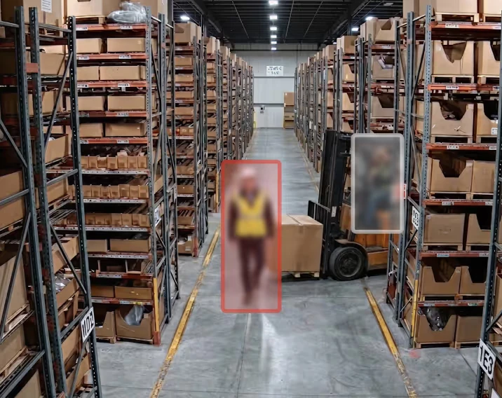 Warehouse aisle with a forklift and two blurred people marked by detection boxes